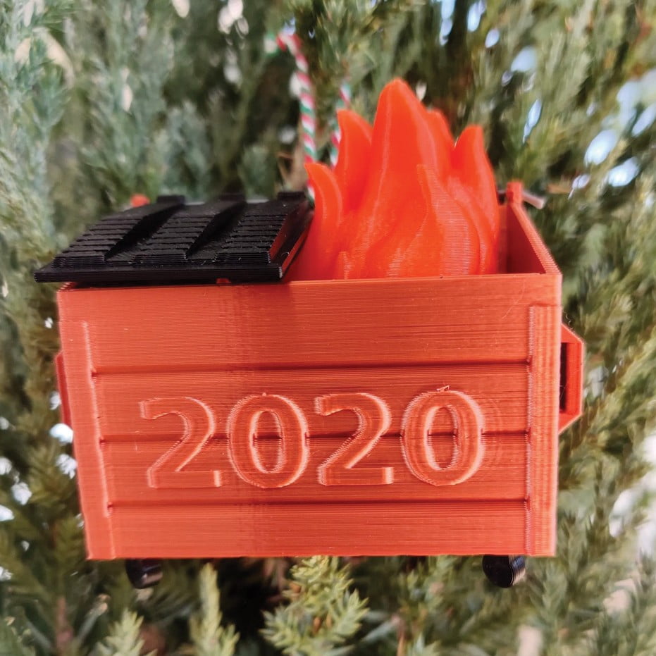 Christmas tree with a red ornament in the shape of a trash dumpster with fire coming out of them, and "2020" on the front. 